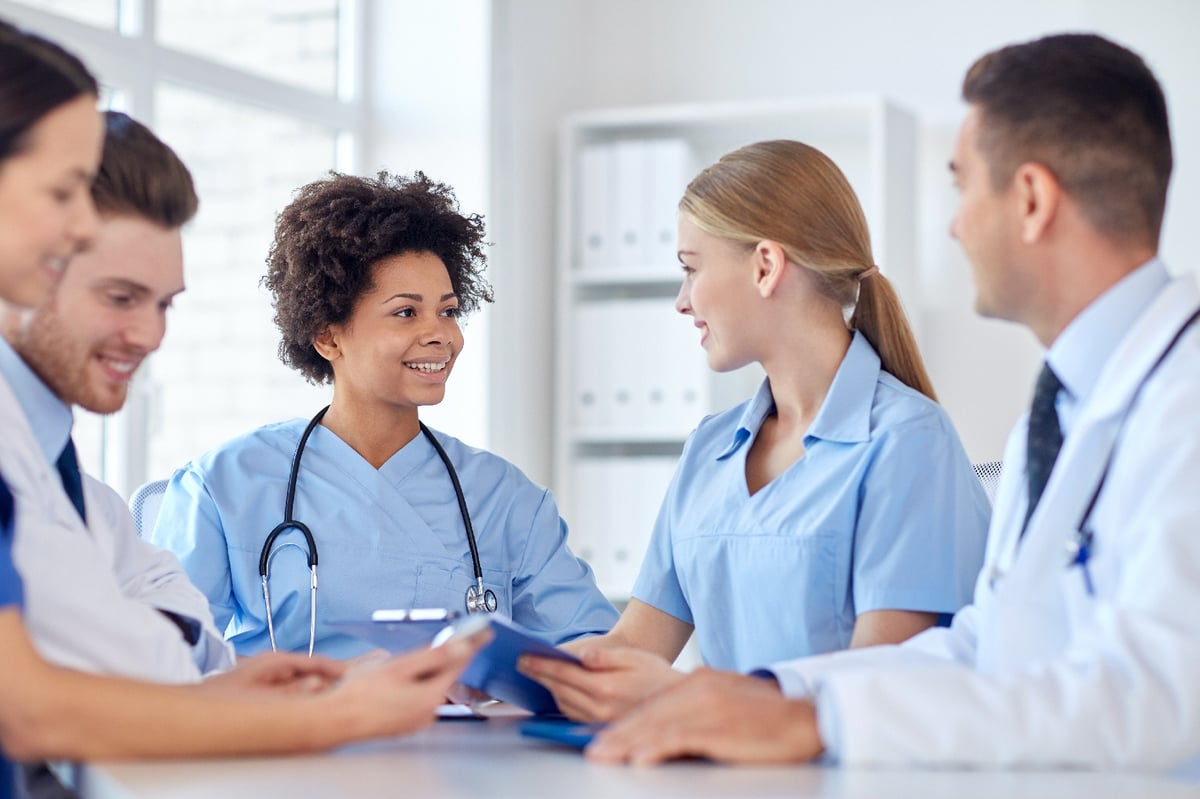 Three nurses smiling at a table with two doctors during a meeting.